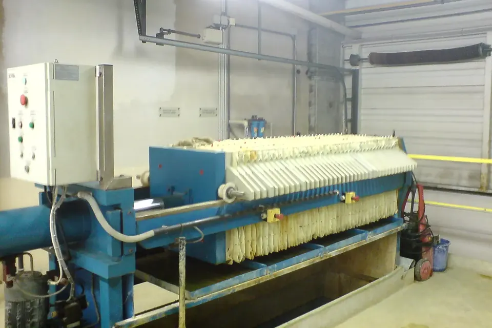 Blau lackierte Kammerfilterpresse mit hellen Filterplatten und Schaltkasten in einer Betriebshalle