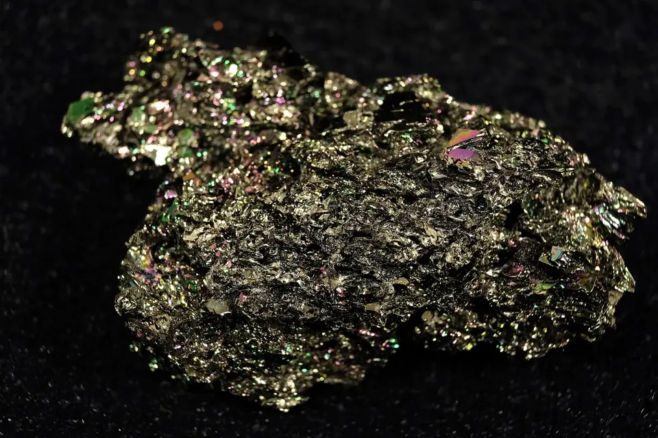 Großer, unregelmäßiger Brocken aus Siliciumcarbid-Kristallen mit metallisch grün-goldenem Schimmer auf schwarzem Grund